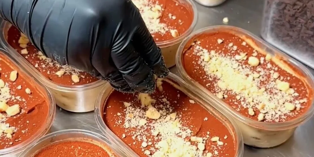 Gloved hands finishing multiple tiramisu portions in a working dessert kitchen